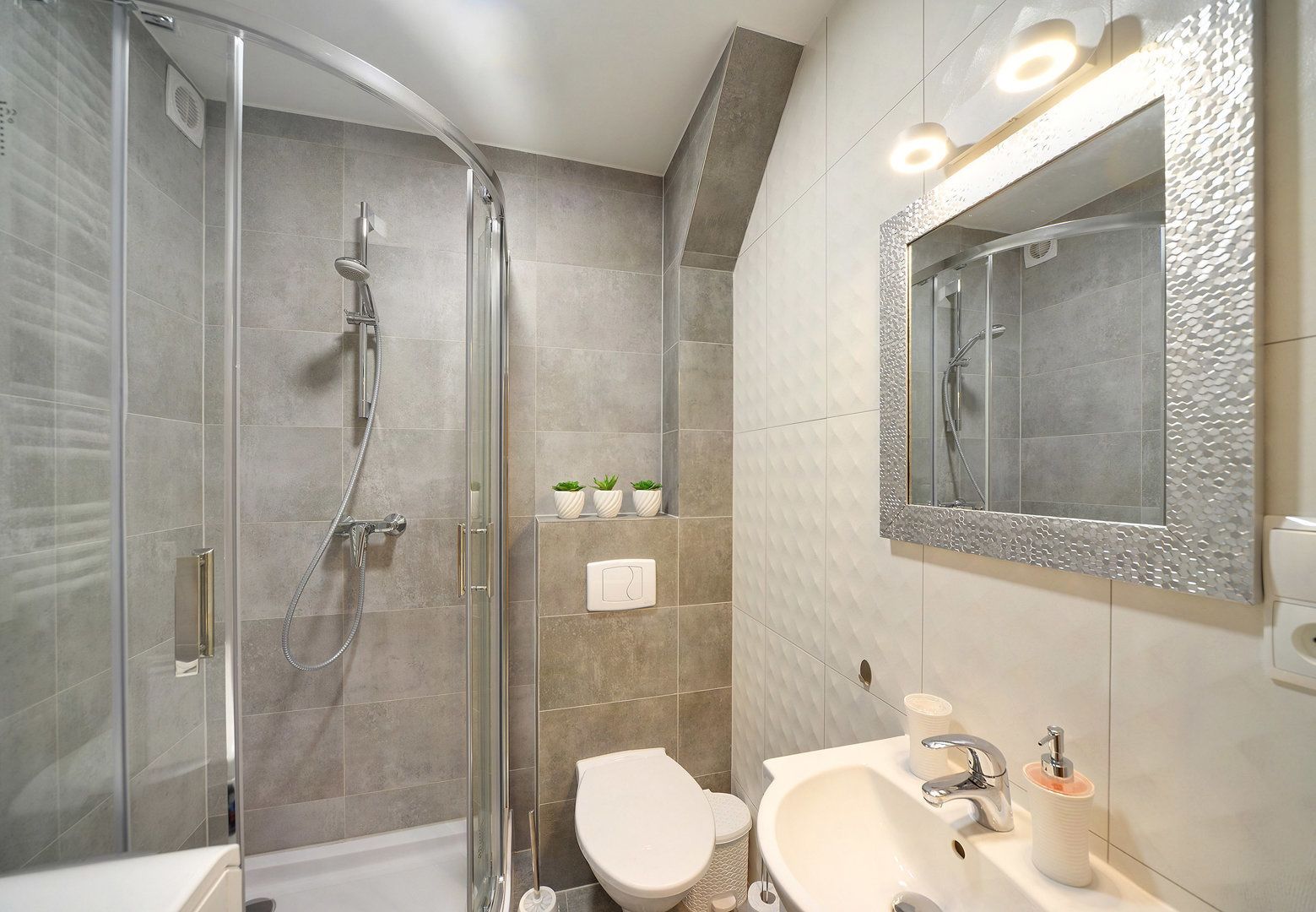 A modern bathroom with a glass-enclosed shower, a toilet, and a sink with a mirror.