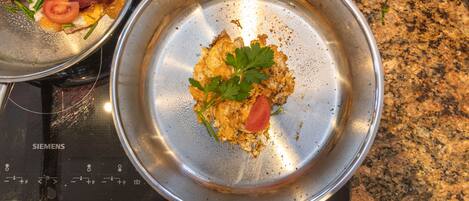 A stainless steel pan on a Siemens induction cooktop with scrambled eggs, a tomato, and green herbs.