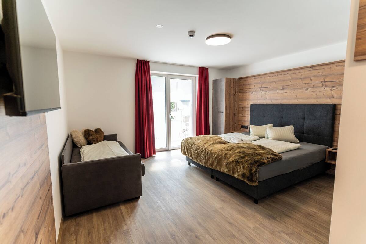 Een moderne slaapkamer met een bed, een bank en een glazen schuifdeur naar een balkon.