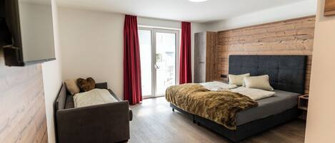 Ein modernes Schlafzimmer mit Bett, Sofa und einer Schiebetür, die auf einen Balkon führt.
