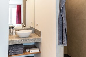 Un baño con lavamanos blanco, encimera de mármol y un perchero.