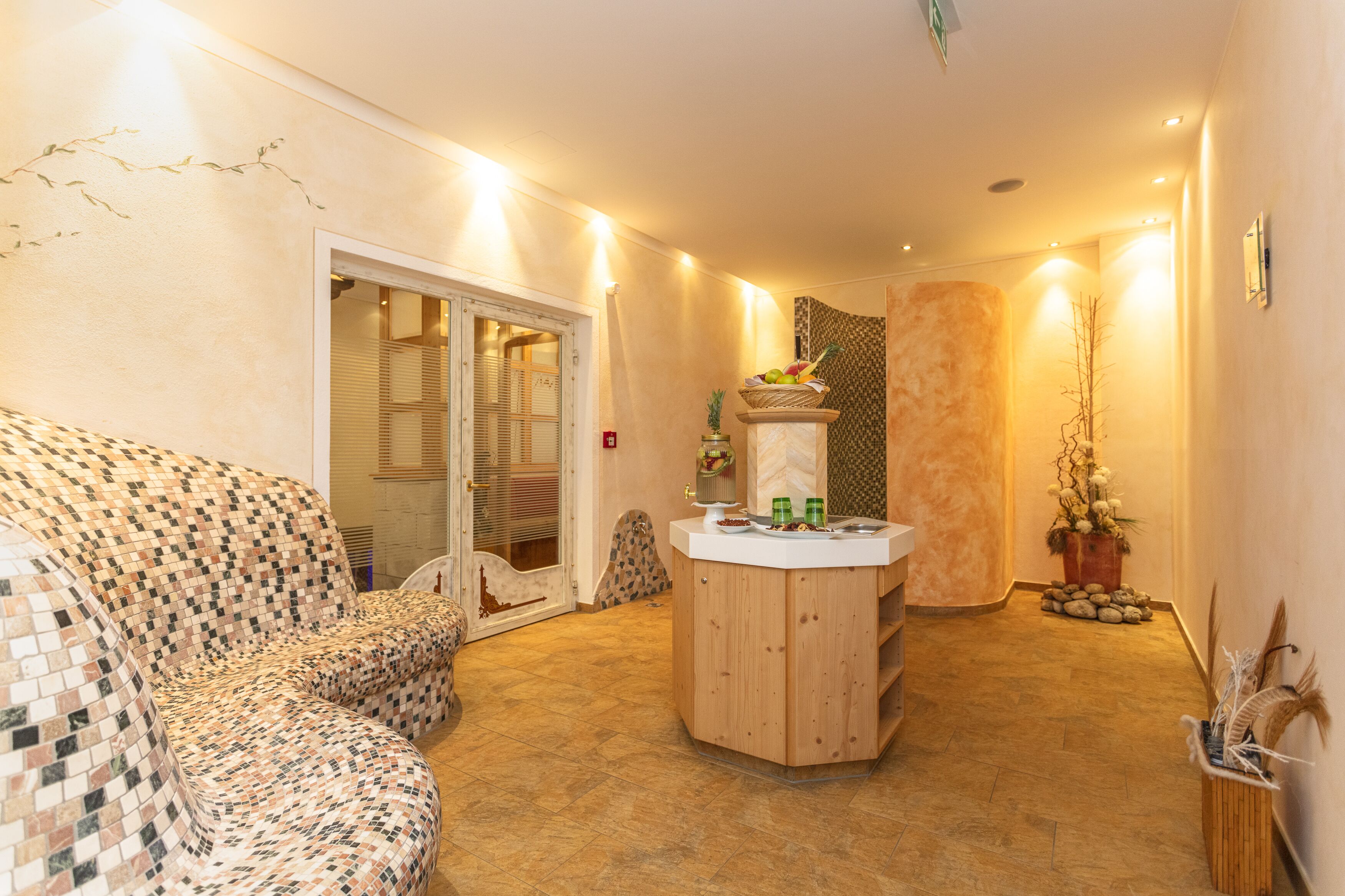 A cozy living area with a patterned sofa, a wooden coffee table with fruit and drinks, and a door leading to a balcony.