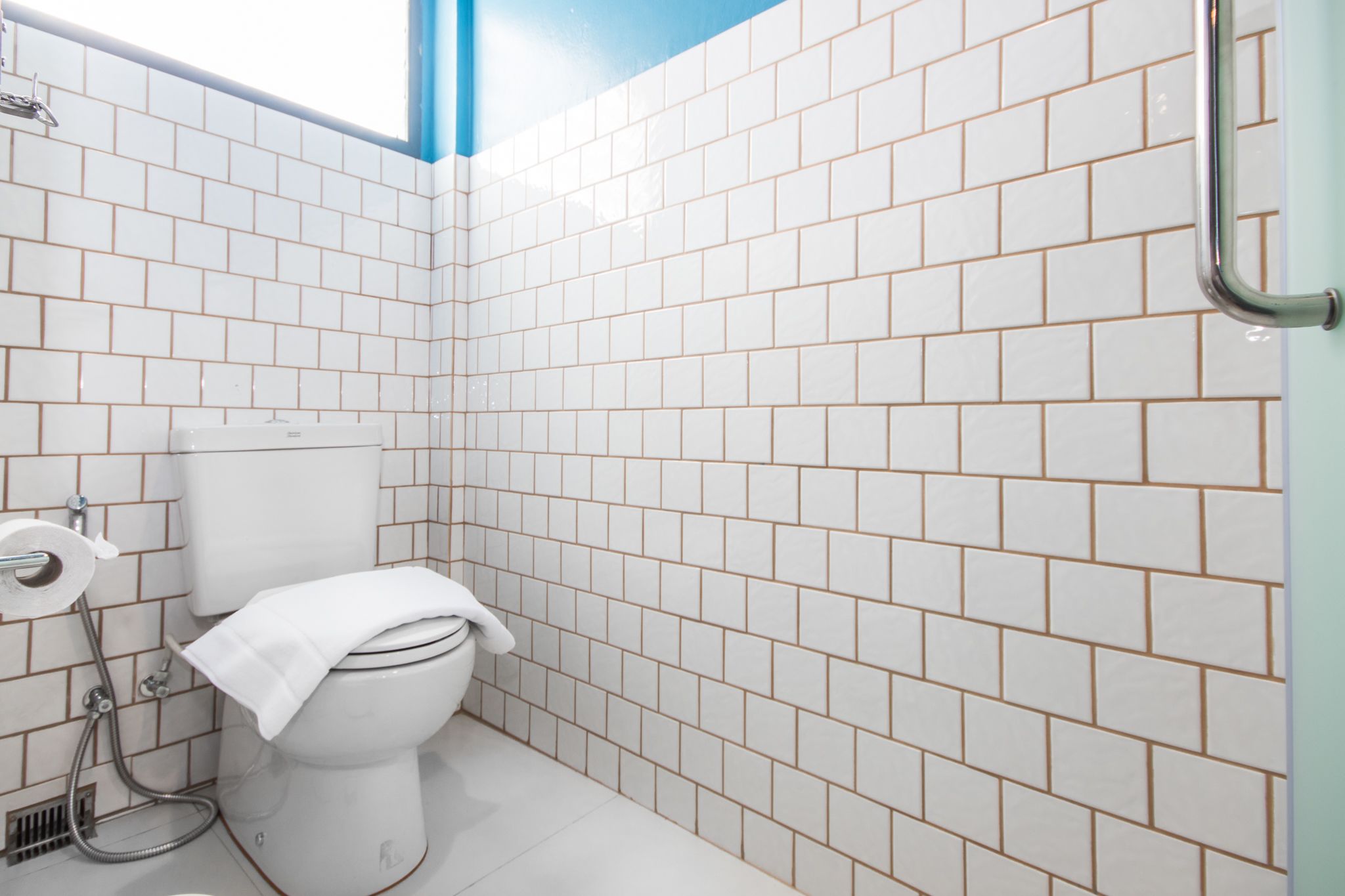 Un baño con paredes de azulejos blancos, inodoro blanco y zona de ducha.
