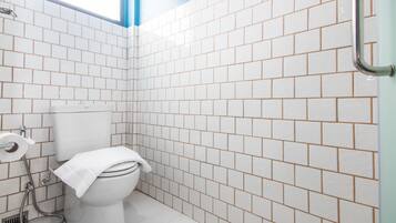 Un baño con paredes de azulejos blancos, inodoro blanco y zona de ducha.