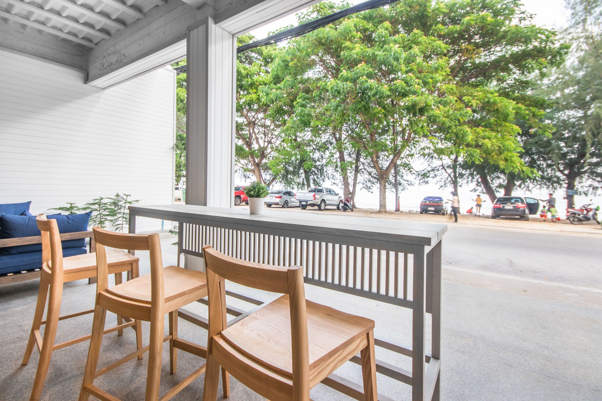 An outdoor seating area with wooden chairs and a table, overlooking a street with parked cars and trees.