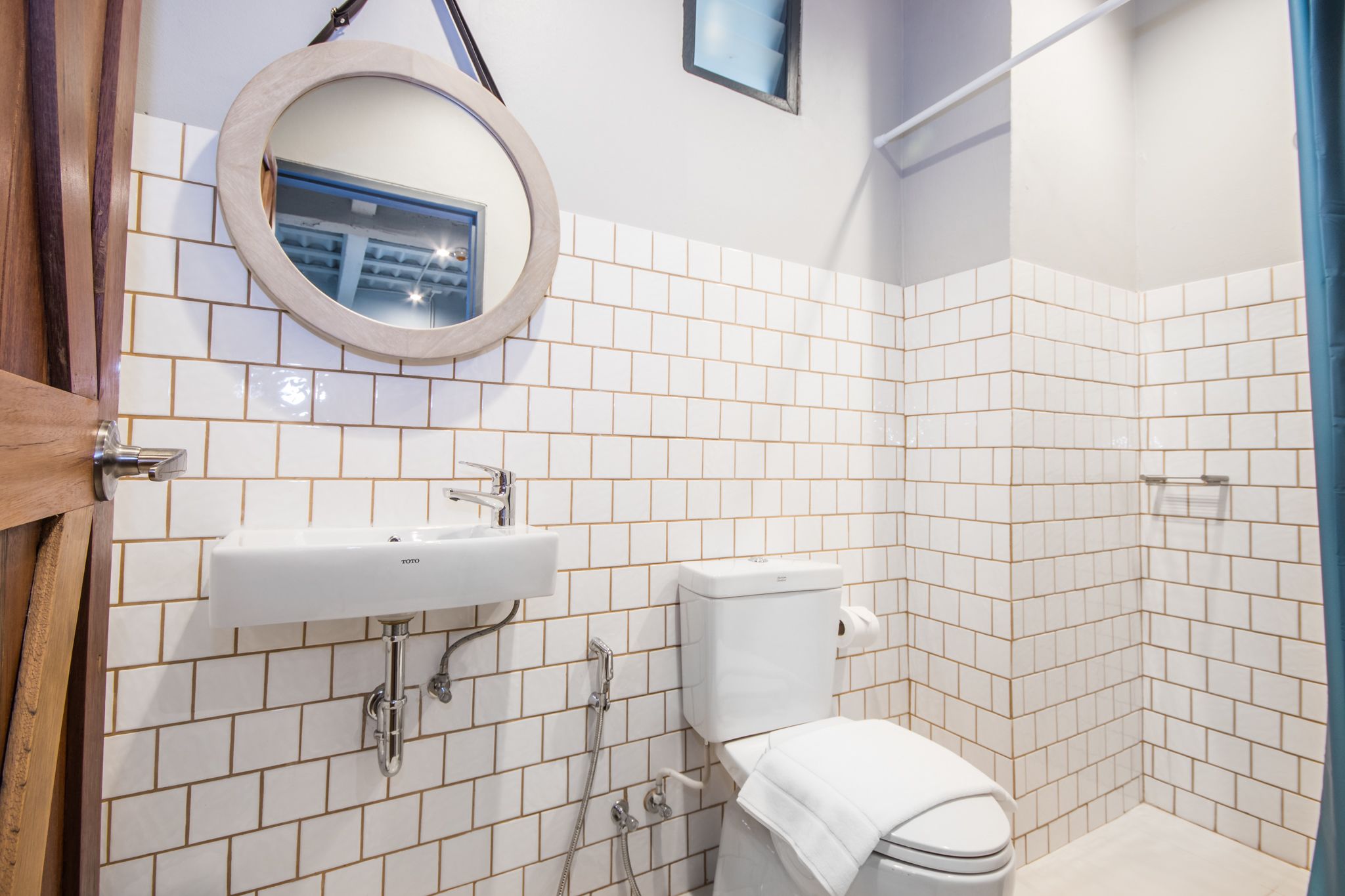 Une salle de bain avec des murs recouverts de carreaux blancs, un lavabo, des toilettes et un espace douche.