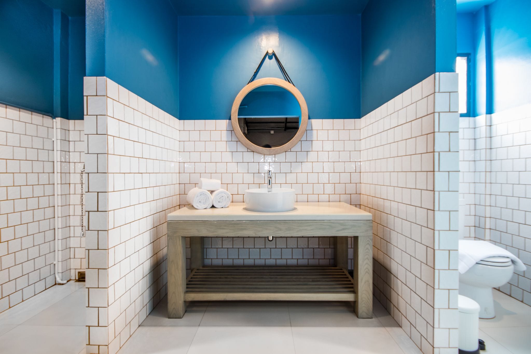 Casa de banho moderna com toucador de madeira, azulejos brancos e uma parede de destaque azul.