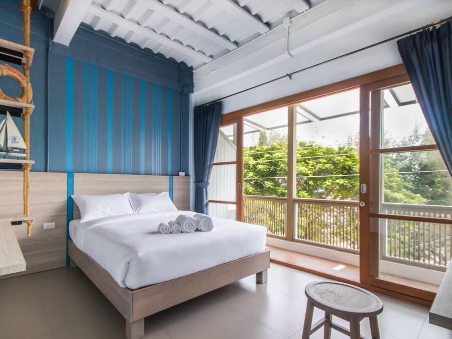 Un dormitorio con cama, una mesita, una silla, un ventanal con vistas a la vegetación y un flotador en la pared.