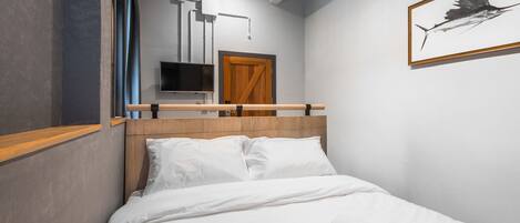Moderni hotellihuone, jossa on puinen sängynpääty, valkoiset vuodevaatteet, seinälle asennettu televisio ja seinällä oleva kehystetty taideteos, jossa on kuvattuna kala.