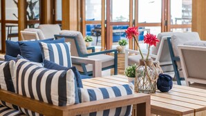 Un área de estar moderna con sofás y sillones a rayas, una mesa de centro de madera y un jarrón con flores rojas.