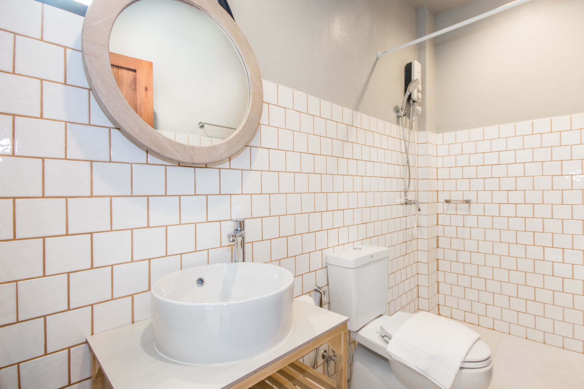 A bathroom with white tiled walls, a round mirror, a sink, a toilet, and a shower.