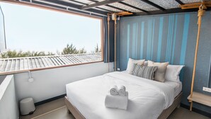 Una cama bien hecha con toallas enrolladas, una ventana con vista al tejado y un columpio de cuerda.