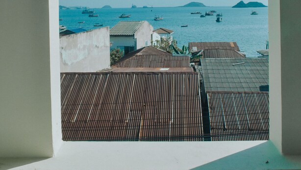 Vista a través de un ventanal arqueado con vista a una zona costera, barcos y edificios.