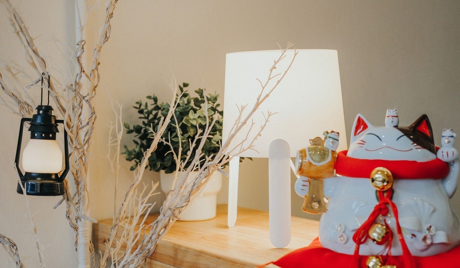 A shelf with a black lantern, a white candle, a potted plant, and a decorative cat figurine.