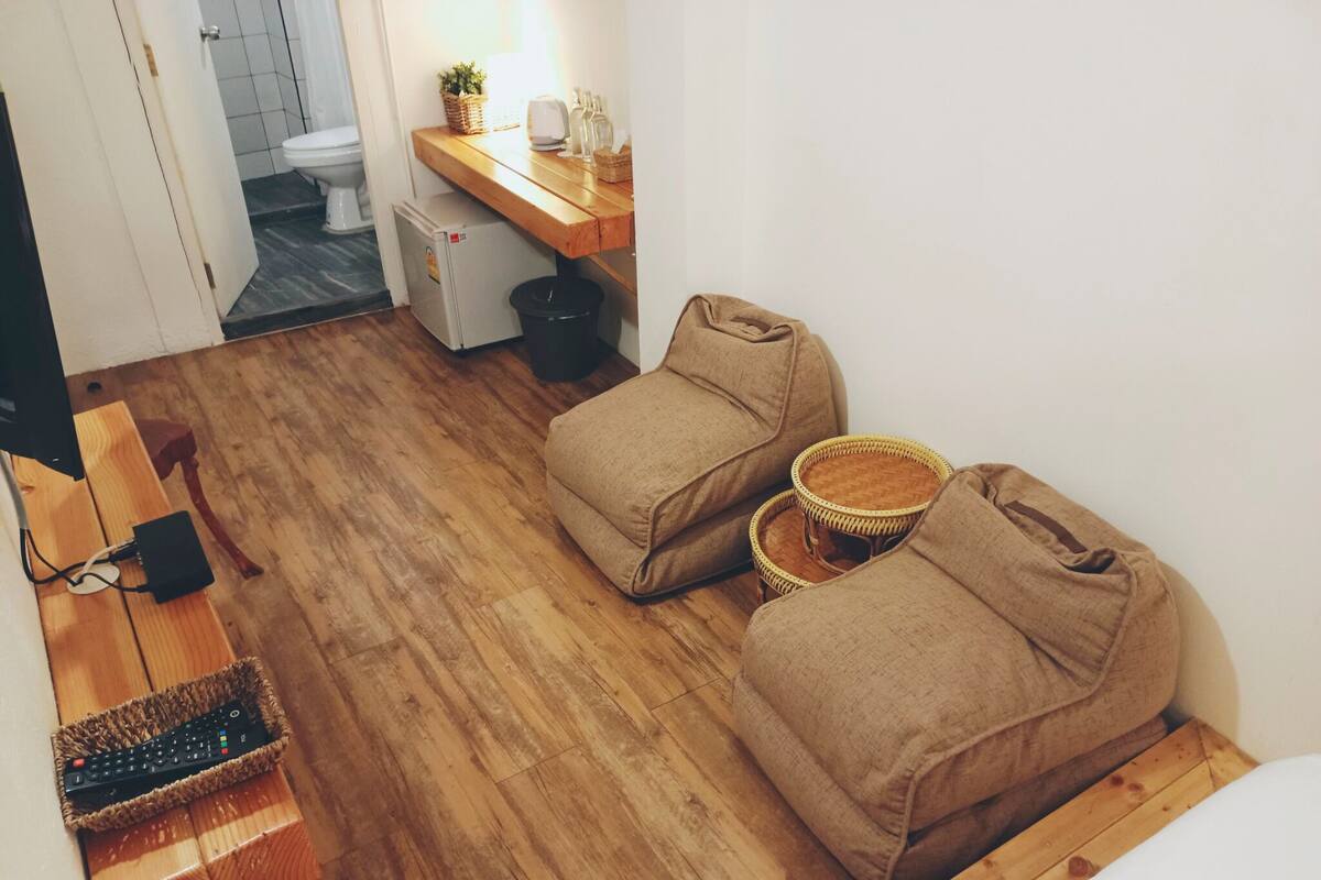 A compact living space with a wooden floor, a small kitchenette, a sofa, and a TV stand with a remote control.