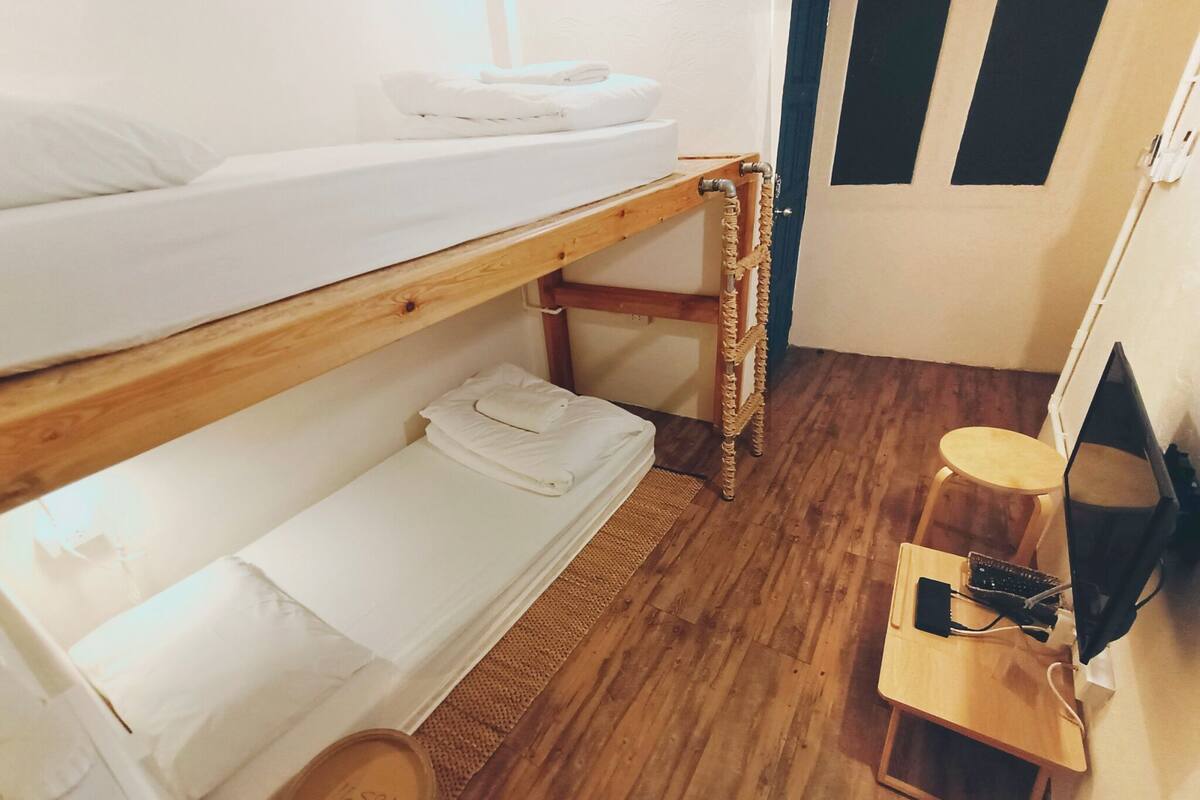 A dormitory room with two bunk beds, a small wooden table with a TV, and a stool.