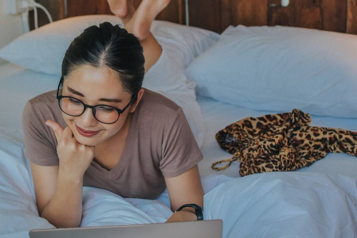 A person lying on a bed with a laptop, a wooden headboard, and a leopard print blanket.