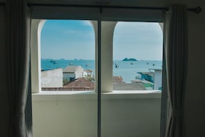 A view from a window with curtains, overlooking a coastal area with boats and buildings.