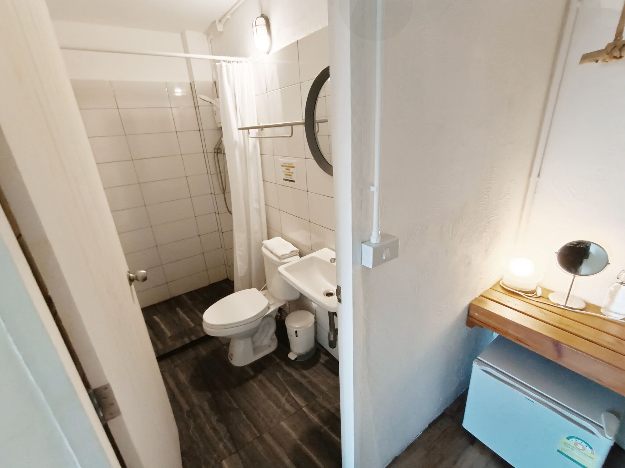 Ein Badezimmer mit Toilette, Bidet und Dusche. Ein kleines Waschbecken und ein Spiegel befinden sich auf einer Holzablage.
