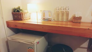 Un área de cocina compacta con refrigerador, cafetera y estante con una cesta, botellas y un cubo de basura.