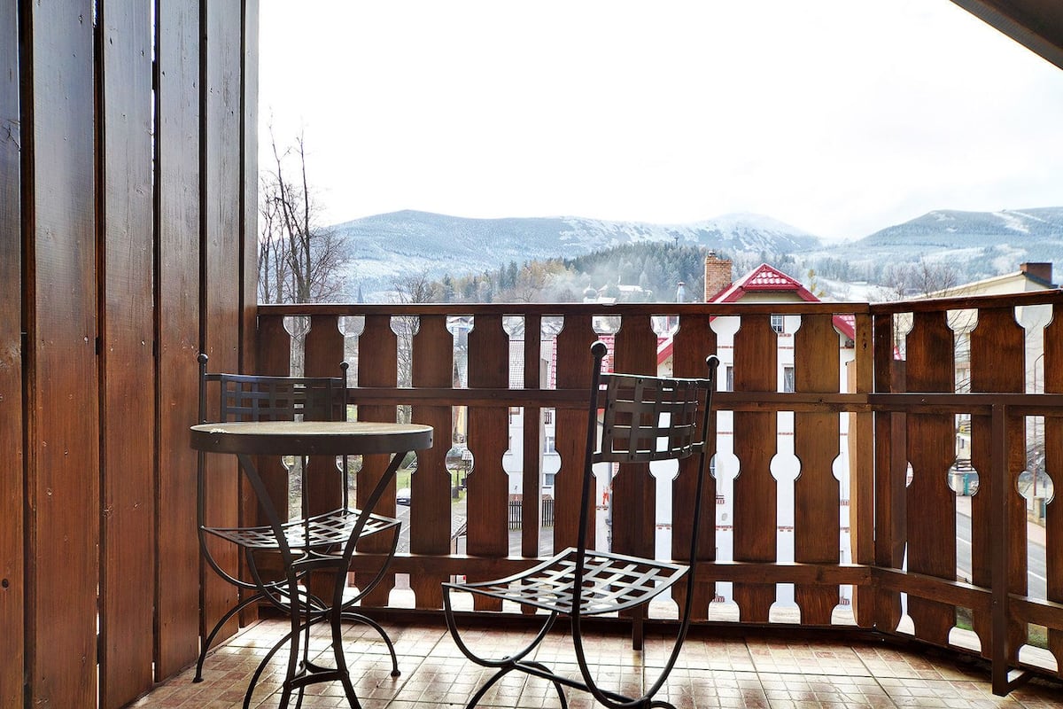 A wooden balcony with a table and two chairs, overlooking a snowy mountain landscape.