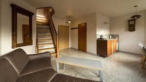 A living room with a brown leather sofa, a wooden staircase, a kitchen area with wooden cabinets, and a dining table. - EverySky Nadrzeczna2 (Karpacz)