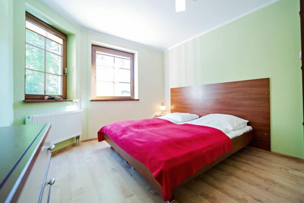 A bedroom with a wooden bed, a radiator, a window, and a desk.