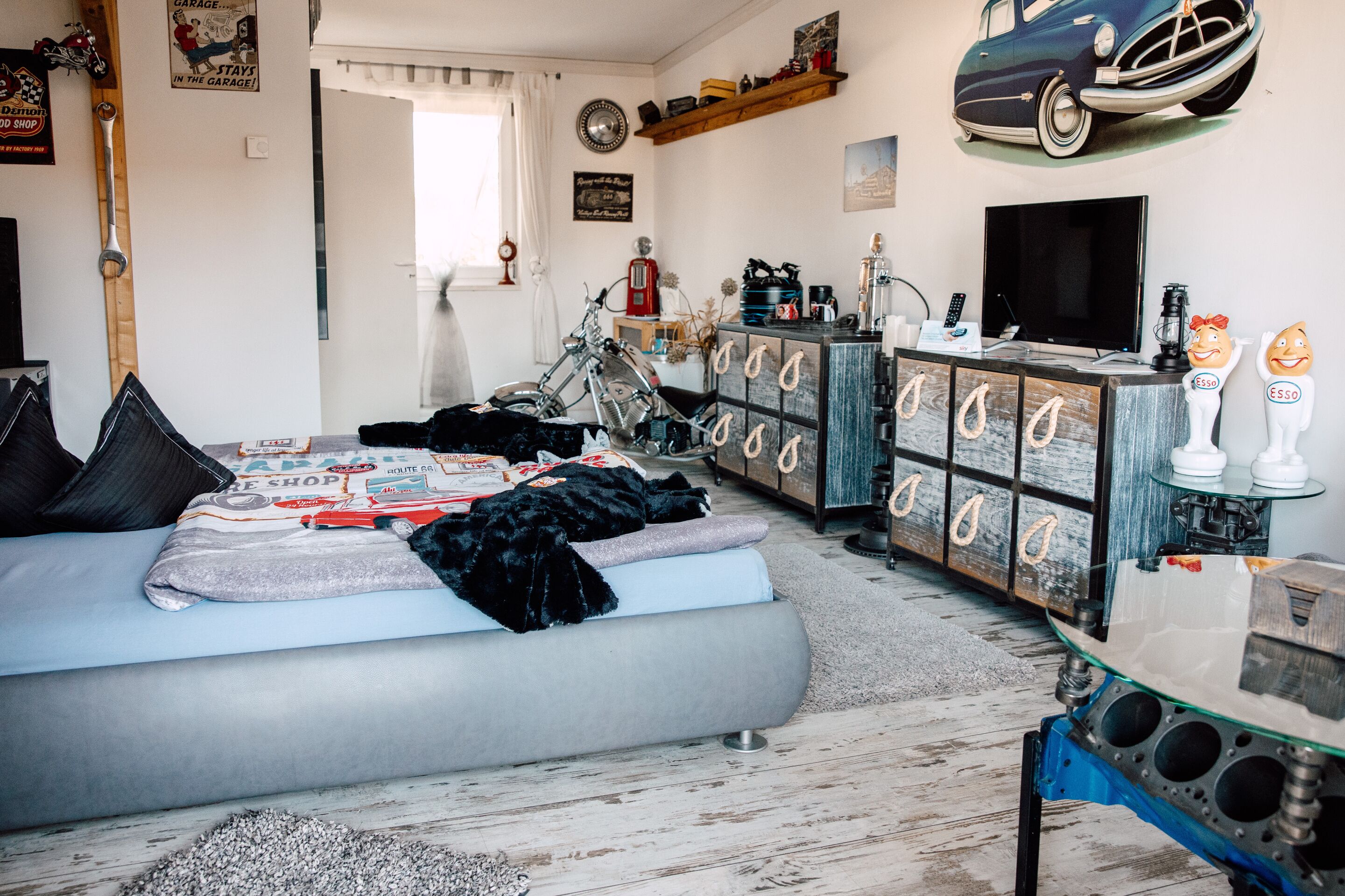 Un dormitorio con cama, motocicleta, televisor y cómoda con varios cajones.