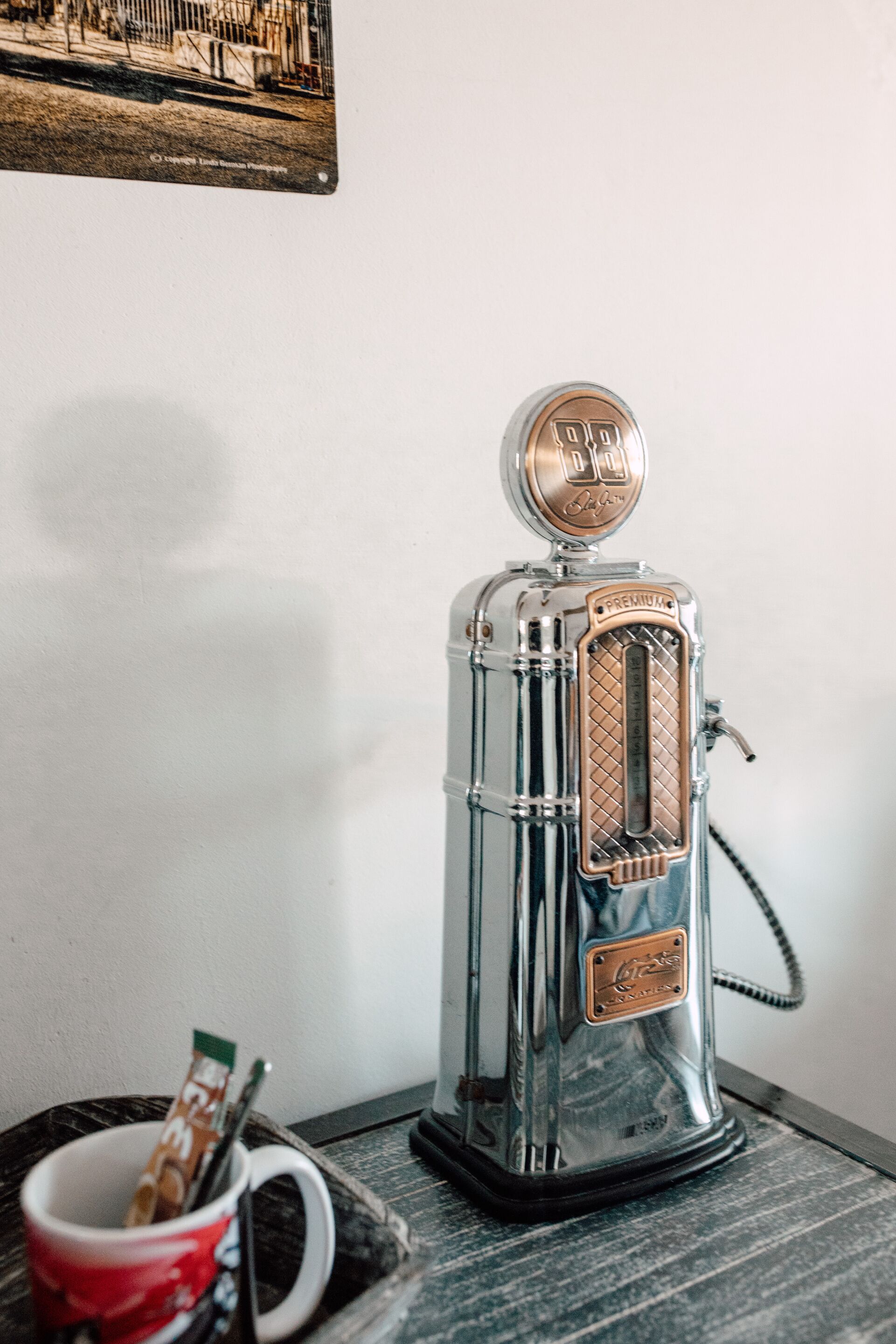 Una cafetera expreso de estilo vintage con cuerpo de vidrio transparente y tapa metálica, sobre una superficie de madera al lado de una taza roja.