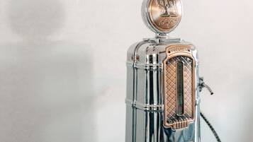 Una cafetera expreso de estilo vintage con cuerpo de vidrio transparente y tapa metálica, sobre una superficie de madera al lado de una taza roja.