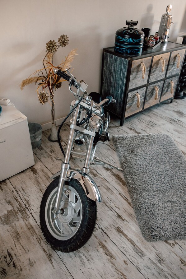 A motorcycle in a room with a wooden floor, a gray rug, and a cabinet with drawers. - Down Town Motel (Berlin)