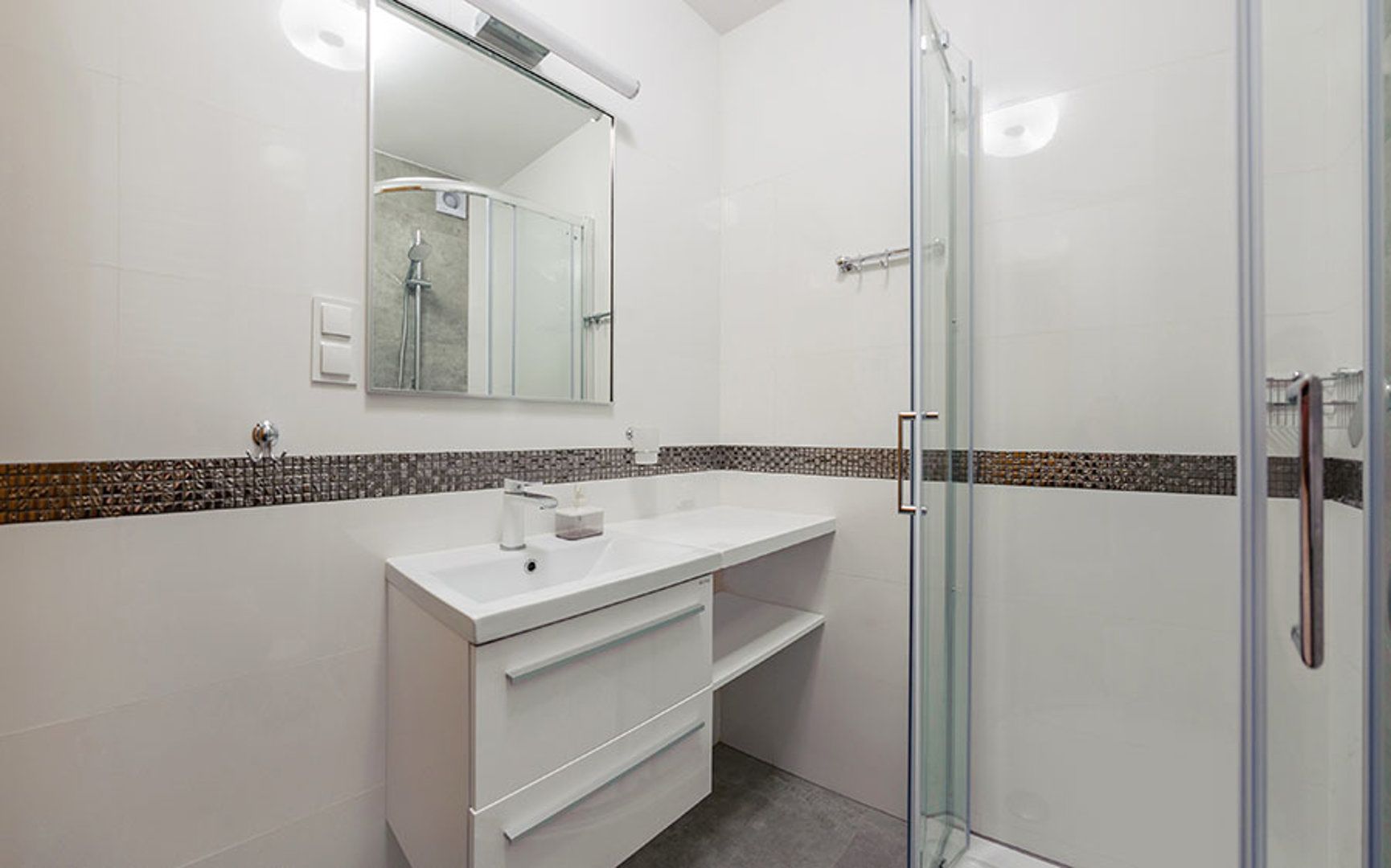 A modern bathroom with a glass shower enclosure, a white sink with a mirror above, and a tiled backsplash.