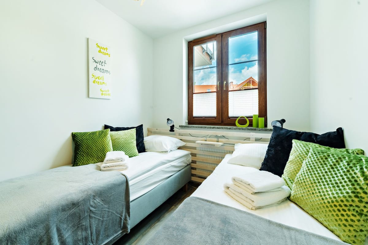 A room with two beds, a window with a view of a house, and a wall with a motivational quote.