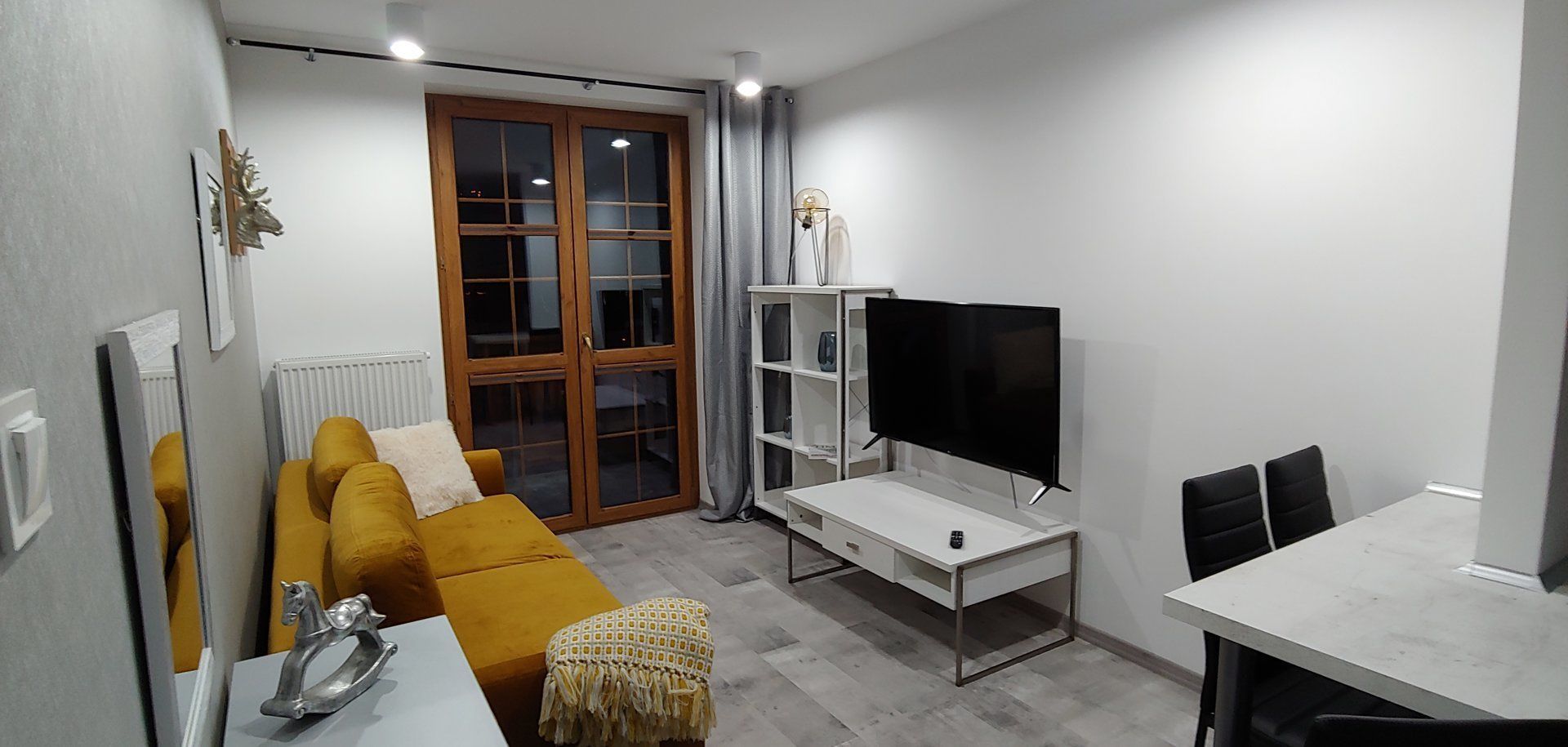 A modern living room with a sofa, a TV, a dining table, and a bookshelf.