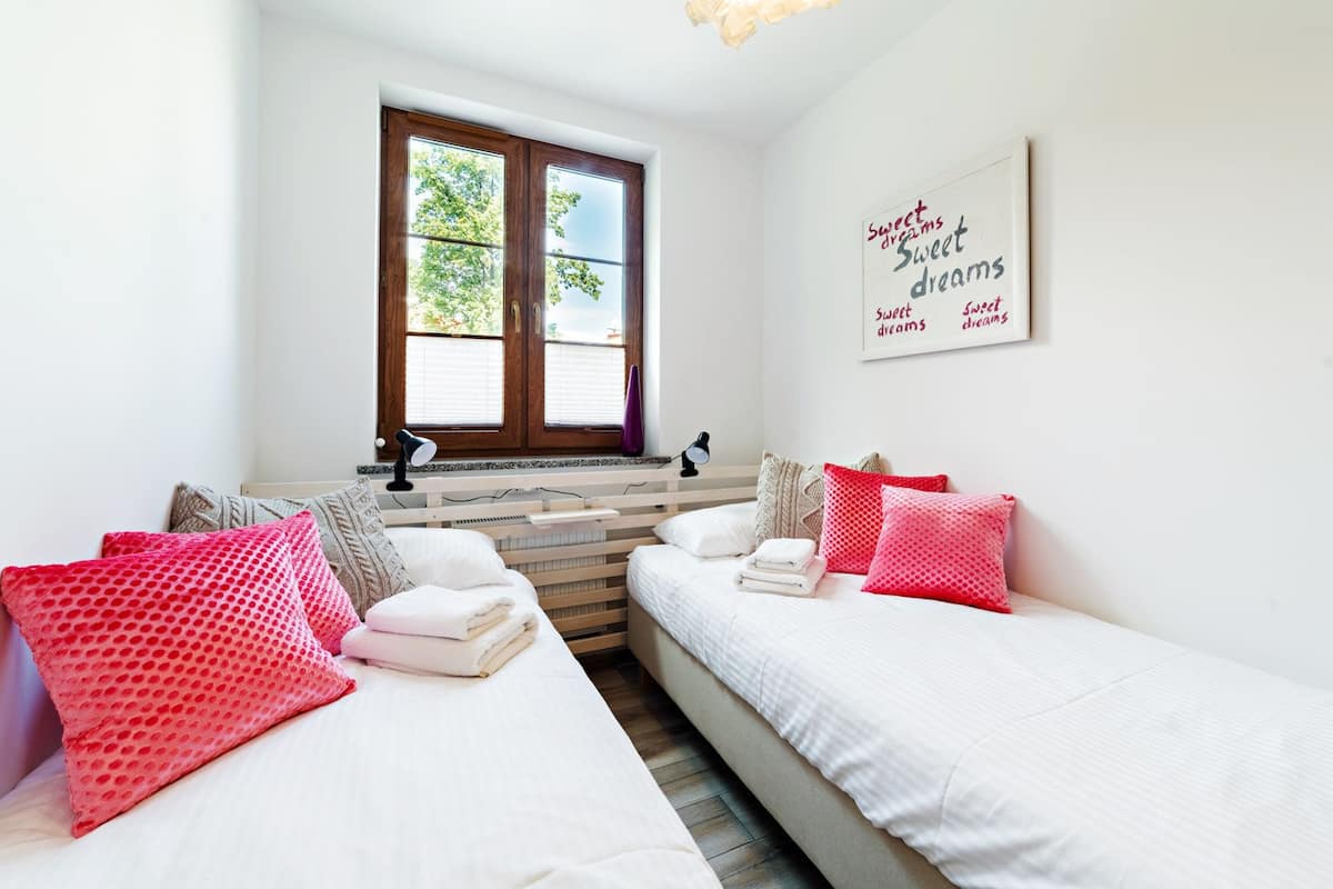 A bedroom with two beds, a window with blinds, a bedside table with lamps, and a wall with a motivational quote.