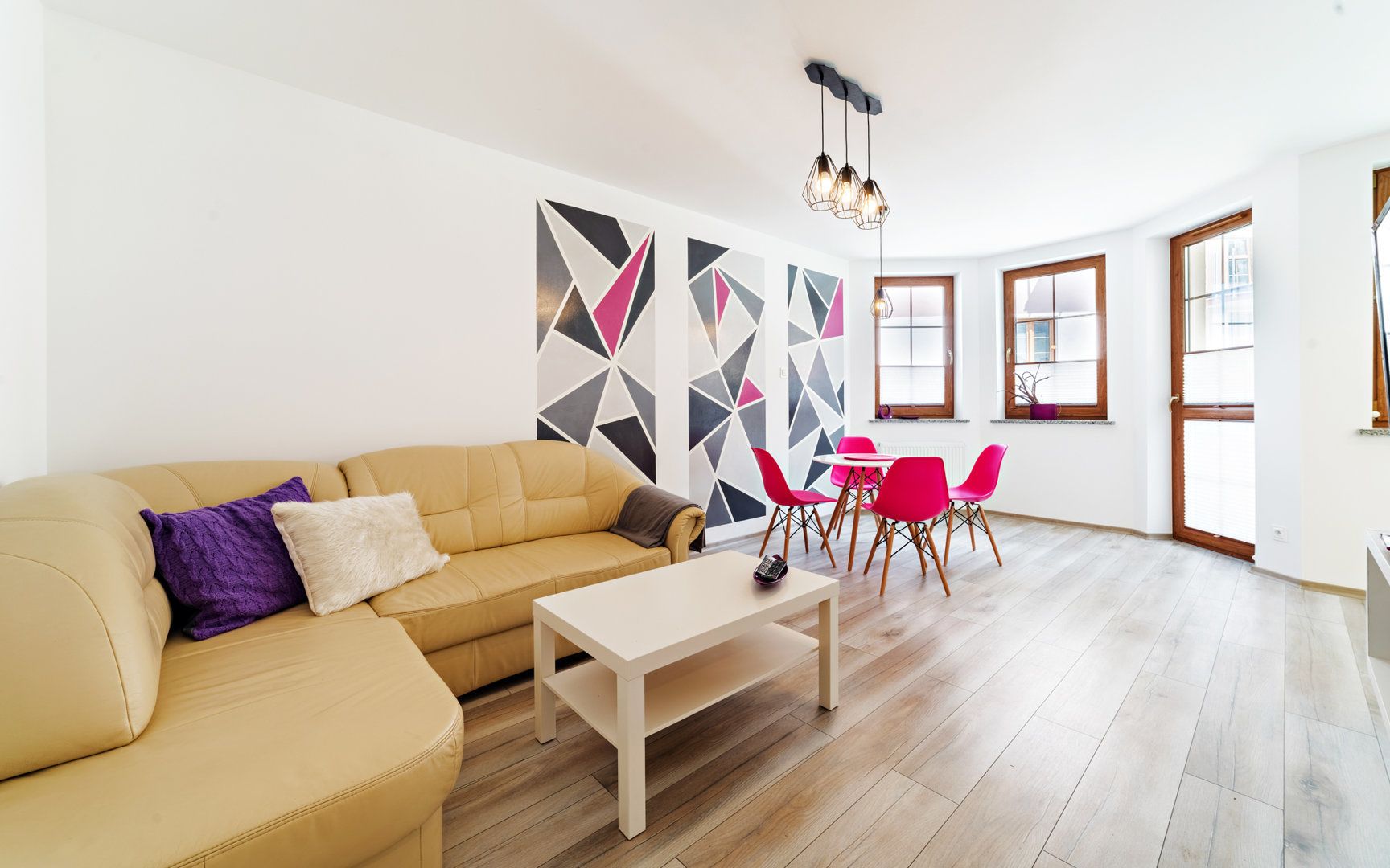 A modern living room with a beige sofa, a coffee table, and a dining area with red chairs.