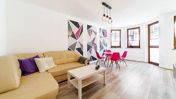 A modern living room with a beige sofa, a coffee table, and a dining area with red chairs.