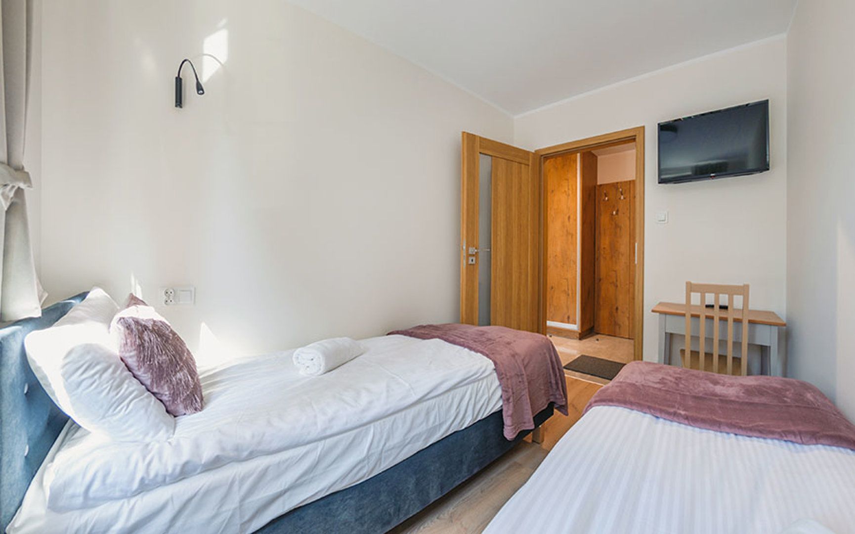 Ein Hotelzimmer mit zwei Betten, einem Fernseher, einer Holztür und einem kleinen Tisch.