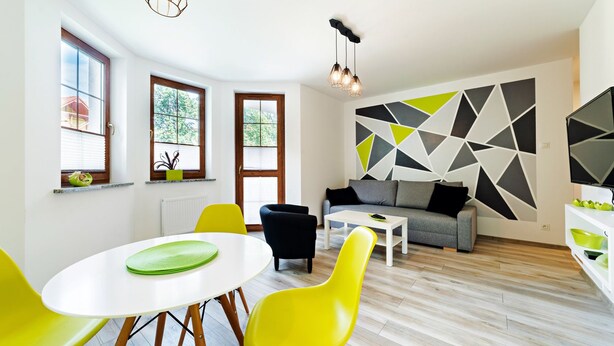 Una sala de estar moderna con un sofá, una mesa de comedor con sillas y una decoración geométrica en la pared.