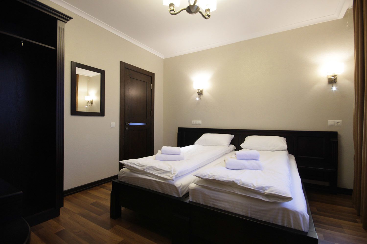 Habitación de hotel con dos camas individuales, un armario de madera oscura, una puerta y una lámpara en el techo.
