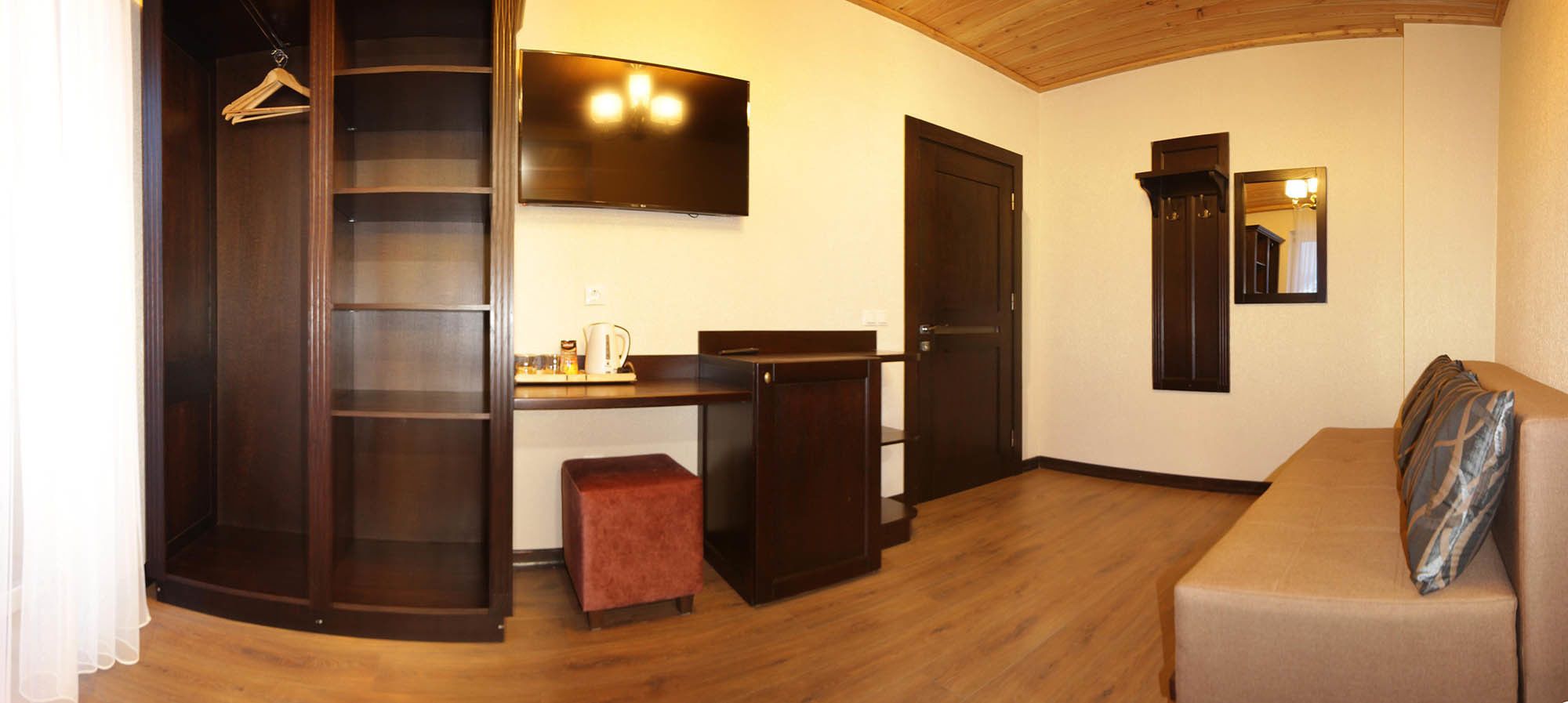 A compact living space with a kitchenette, a sofa, a small table, a TV, and a wardrobe.