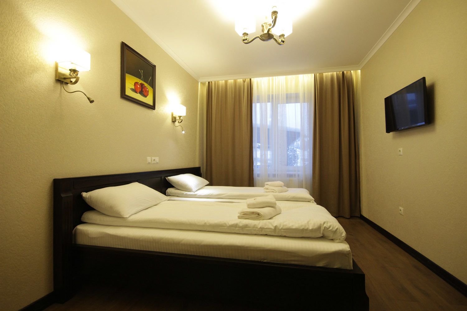 A hotel room with a bed, two wall-mounted lights, a flat-screen TV, and a window with curtains.