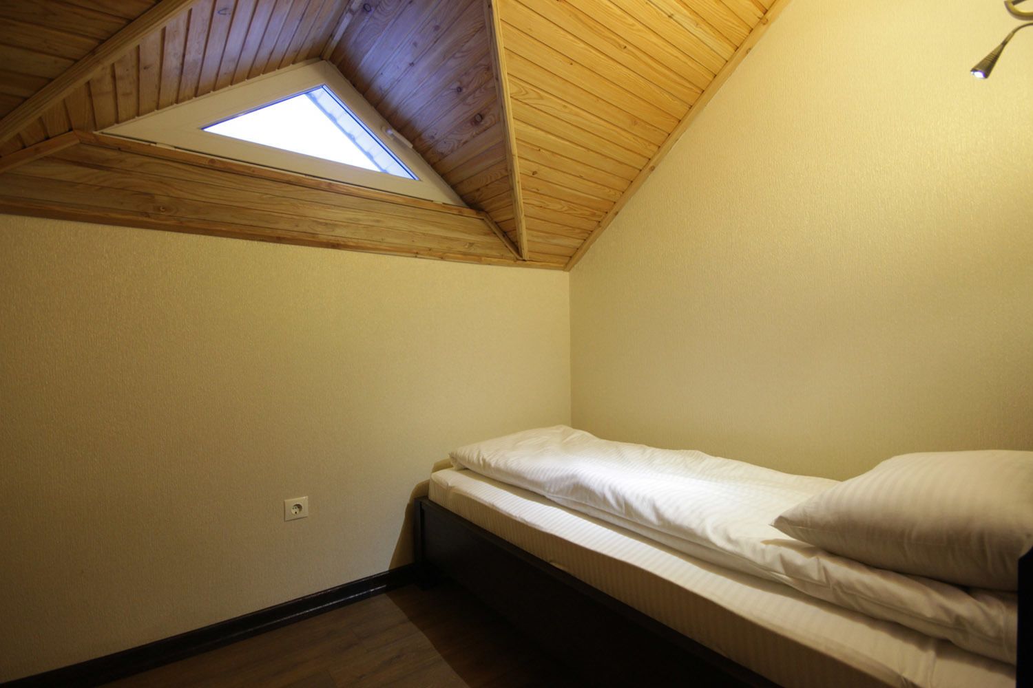 Una habitación pequeña con una cama individual, techo de madera inclinado y tragaluz.
