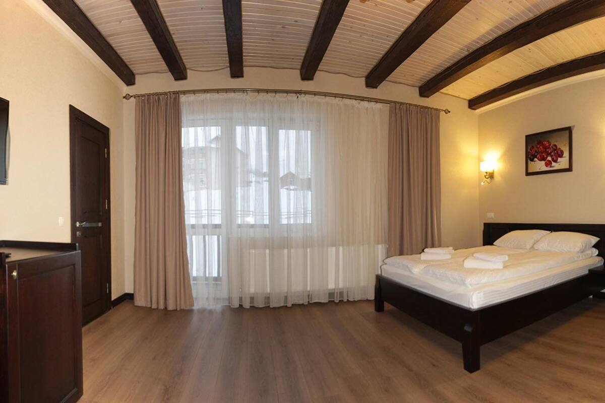 A hotel room with a bed, a desk, a TV, and a window with curtains.