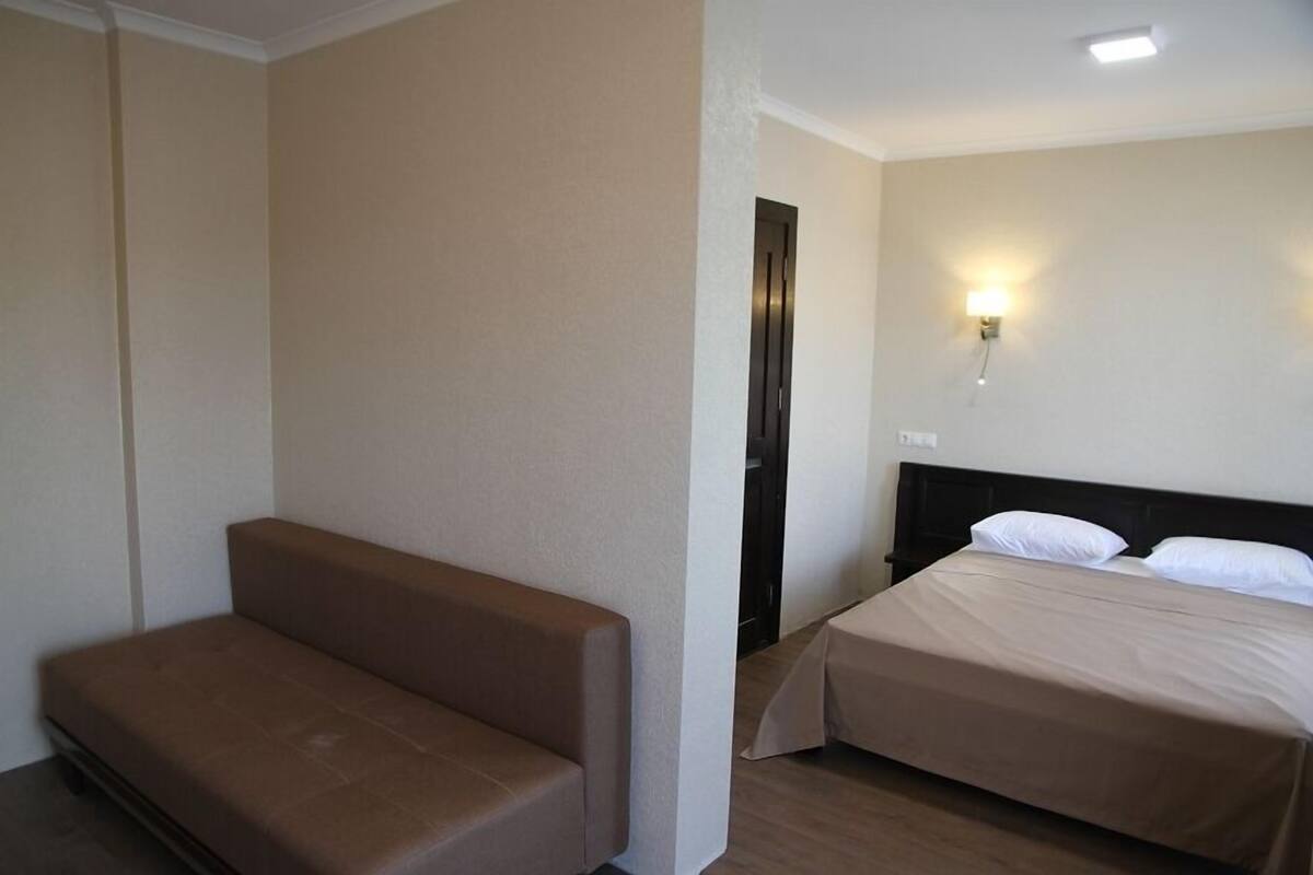A hotel room with a single bed, a small sofa, and a wall-mounted light fixture.