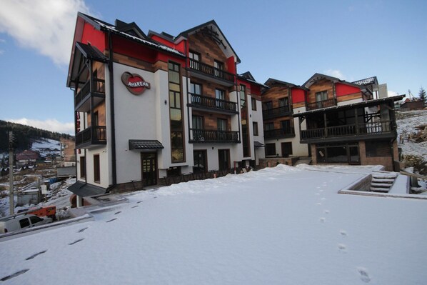 A multi-story hotel with a prominent 'AMARENA' sign, balconies, and a snowy outdoor area. - Amarena (Bukovel)