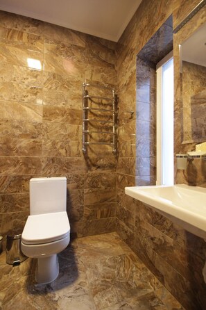 A bathroom with a marble floor, a white toilet, a glass shower enclosure, and a white sink. - Amarena (Bukovel)