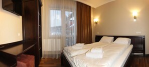 A hotel room with a bed, a TV, a desk, and a window with curtains. - Amarena (Bukovel)