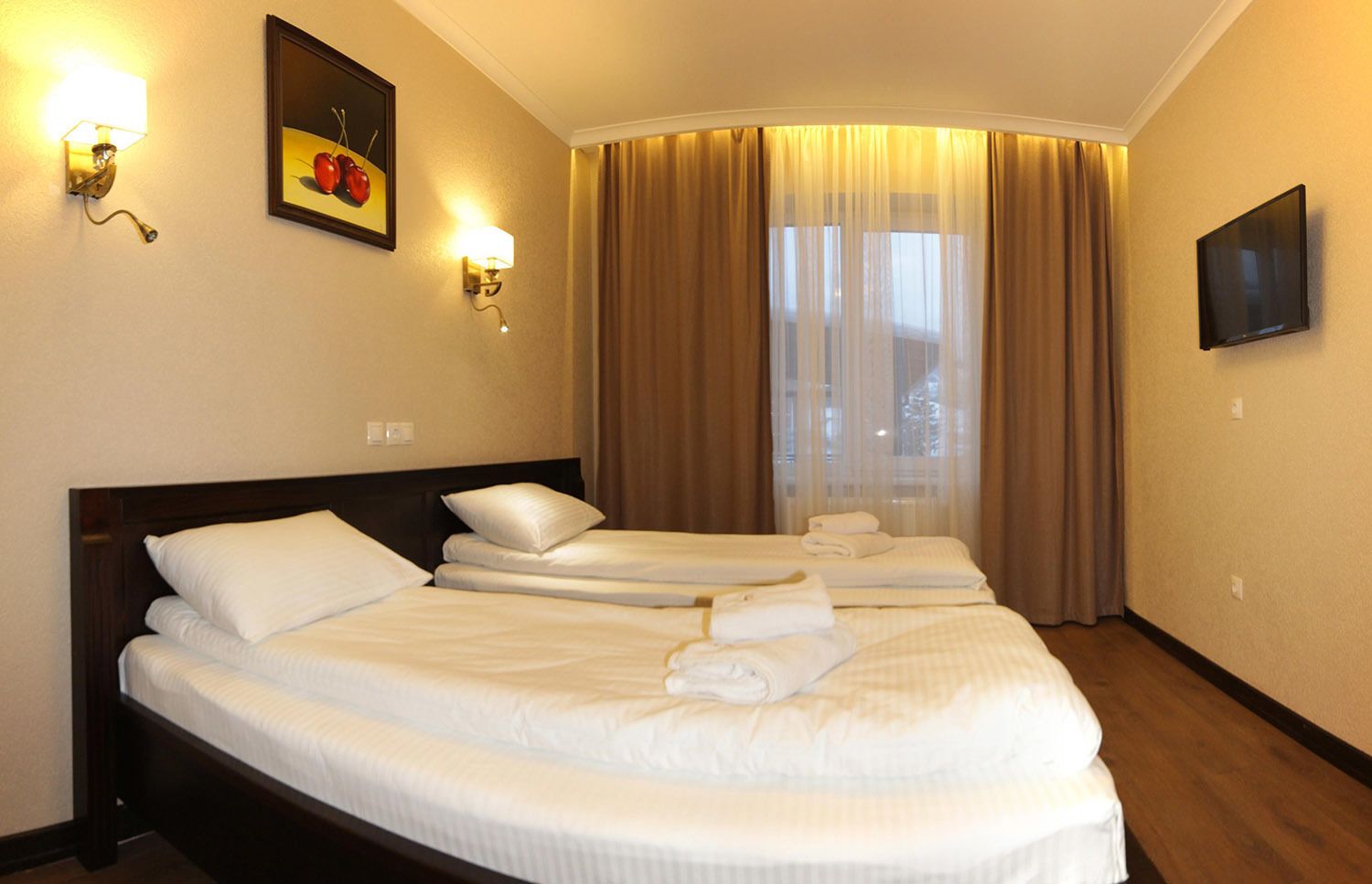 A hotel room with a large bed, two smaller beds, a flat-screen TV, and a window with curtains.