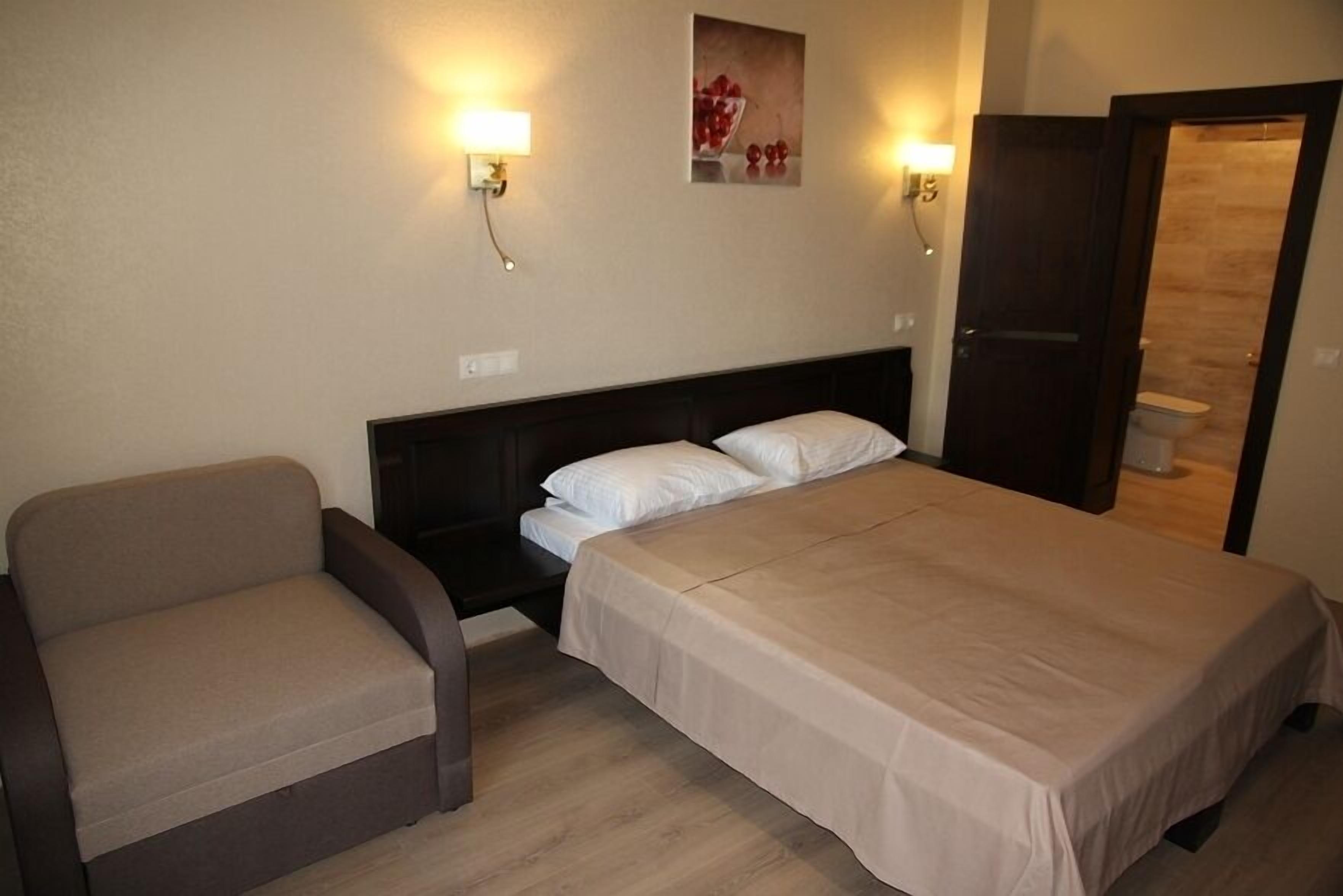 A hotel room with a bed, a sofa, and a small table. There are wall-mounted lights and a picture on the wall.